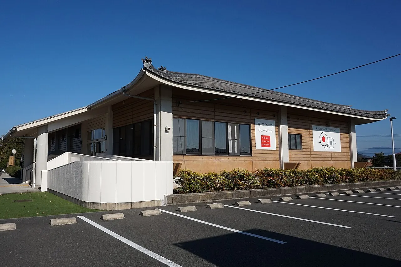 青空の下に建つ、瓦屋根の平屋のマンガミュージアムの建物と駐車場