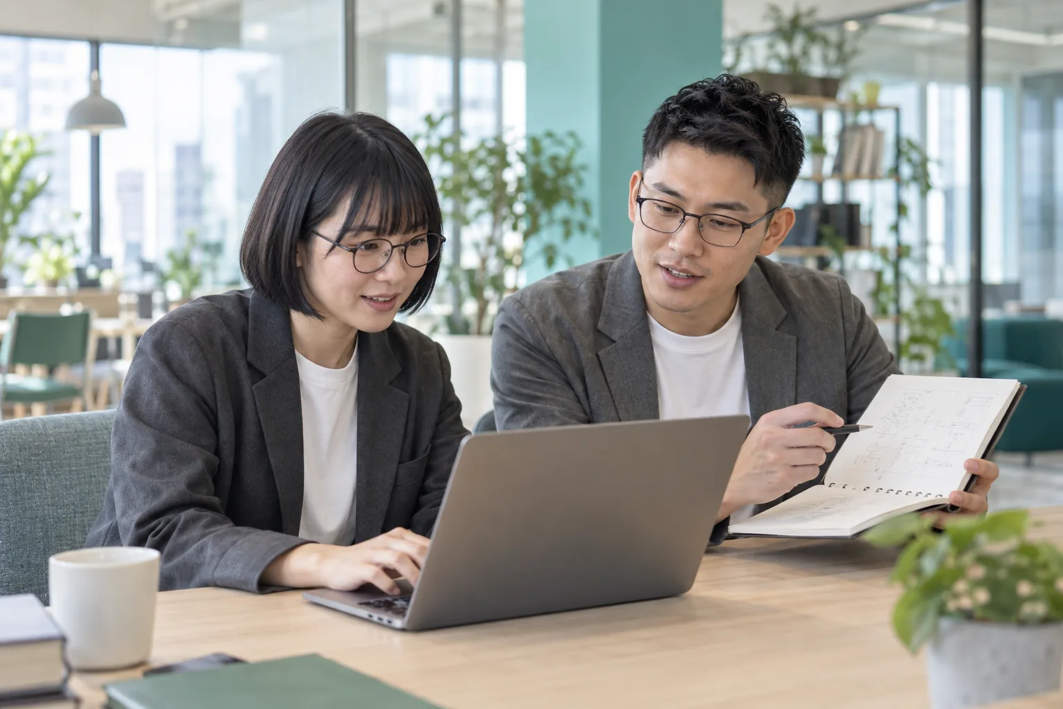 眼鏡をかけた二人が、パソコンとノートを使って一緒に考えるITの仕事のイメージ
